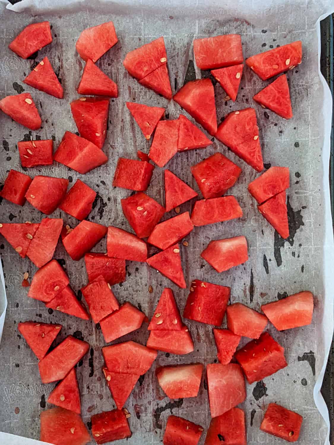 bite size watermelon cubes spread out on a sheet pan lined with parchment paper.