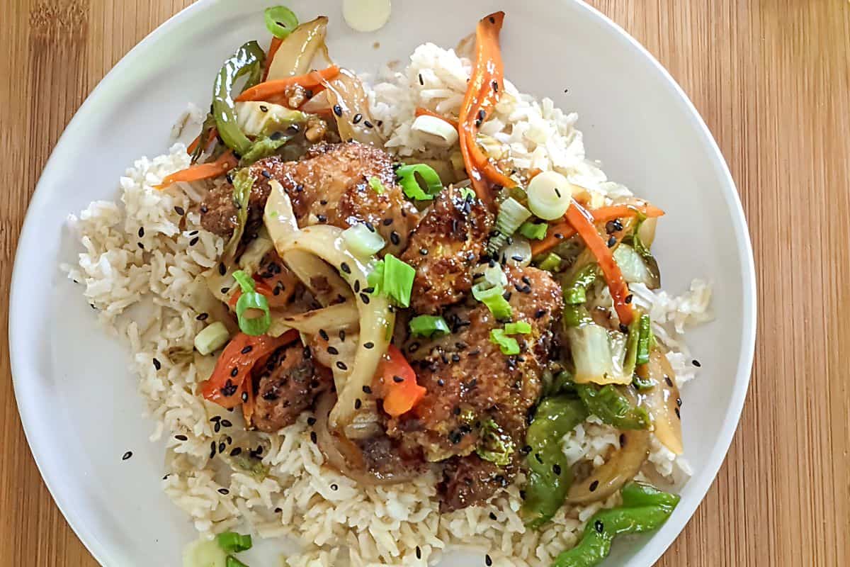 stir fried Hot Honey Sesame Chicken and vegetables on a bed of white rice on a plate.