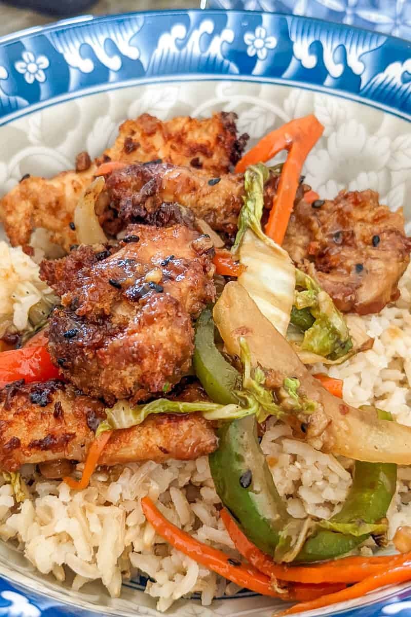 a close up of sesame chicken stir-fry on rice in a bowl