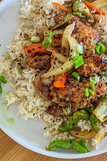 stir fried Hot Honey Sesame Chicken and vegetables on a bed of white rice on a plate.