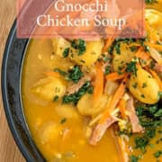 Delicious Pumpkin Gnocchi Chicken Soup in a black bowl, garnished with parsley on wooden surface.