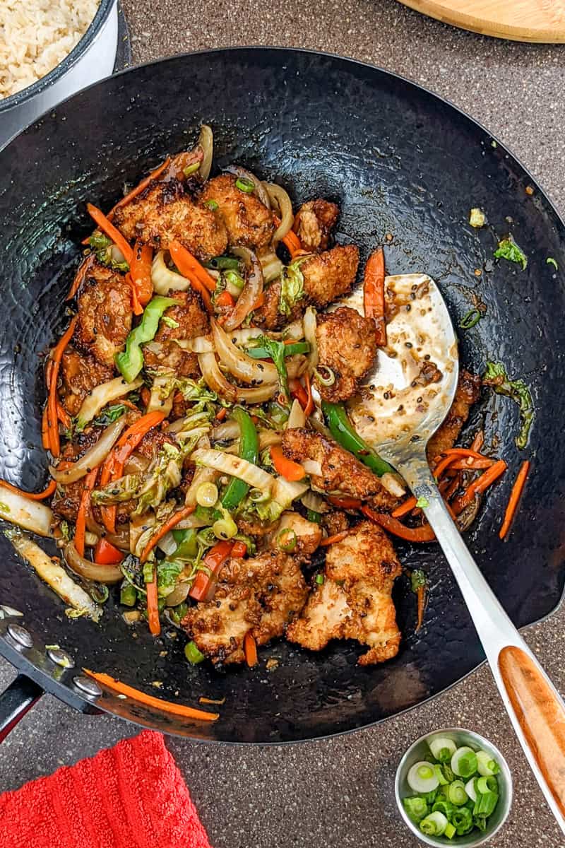 stir fried hot honey sesame chicken and vegetables in a wok.