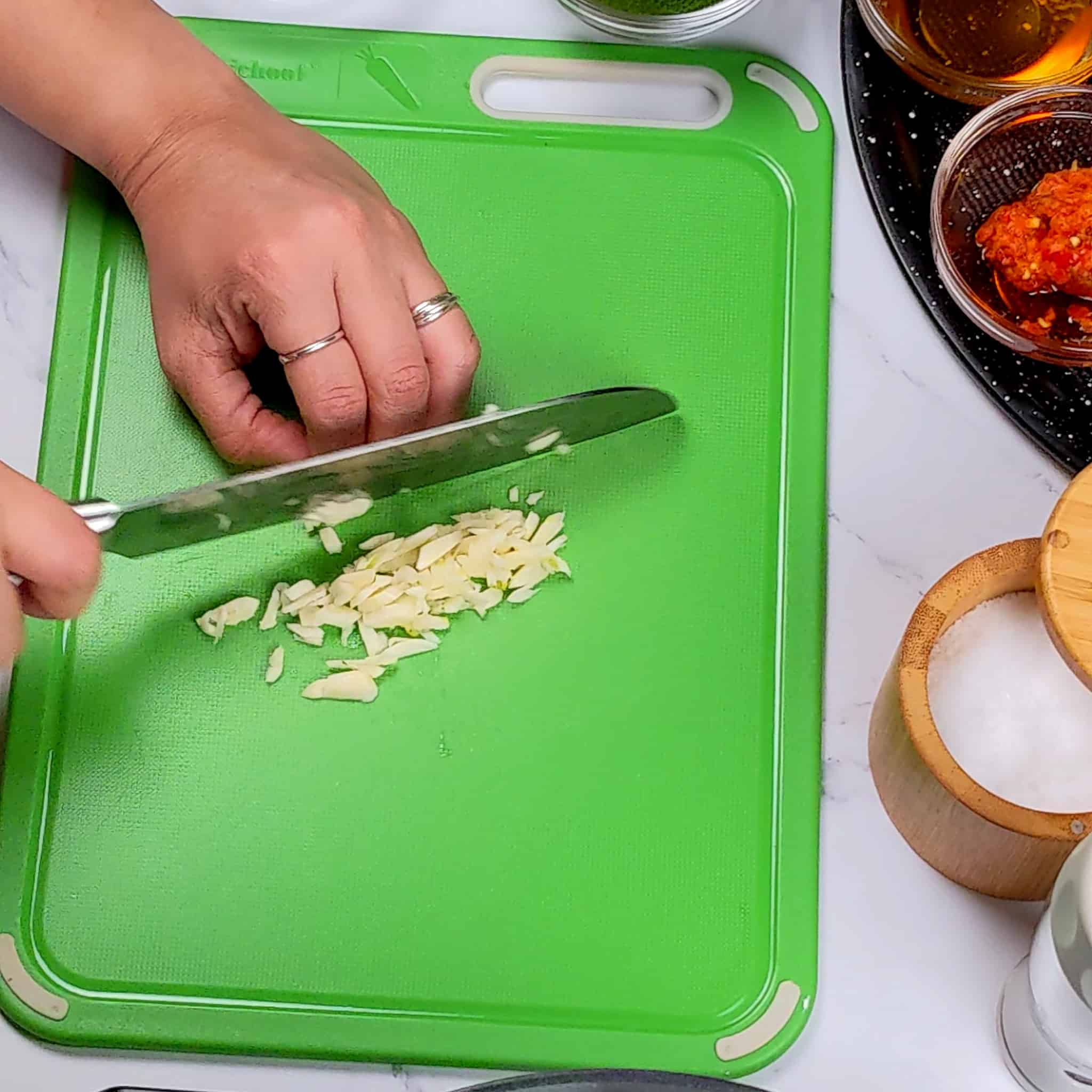 a knife chopping garlic on a plastic cutting board.