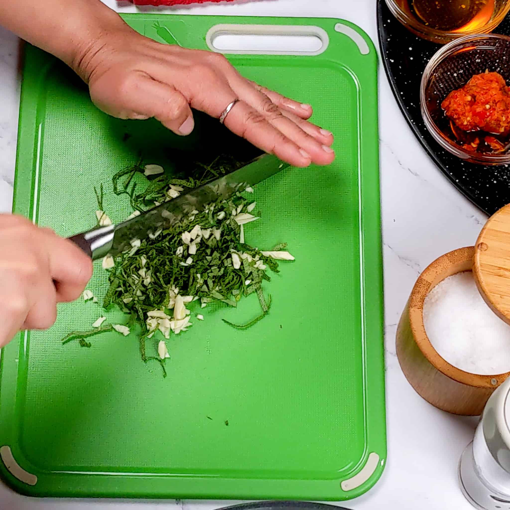 a knife chopping herbs and garlic on a plastic cutting board