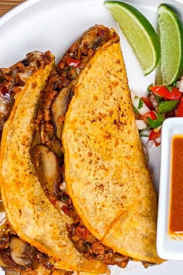 vegetarian mushroom stuffed birria tacos on a plate with consume, lime wedges and pico de gallo.