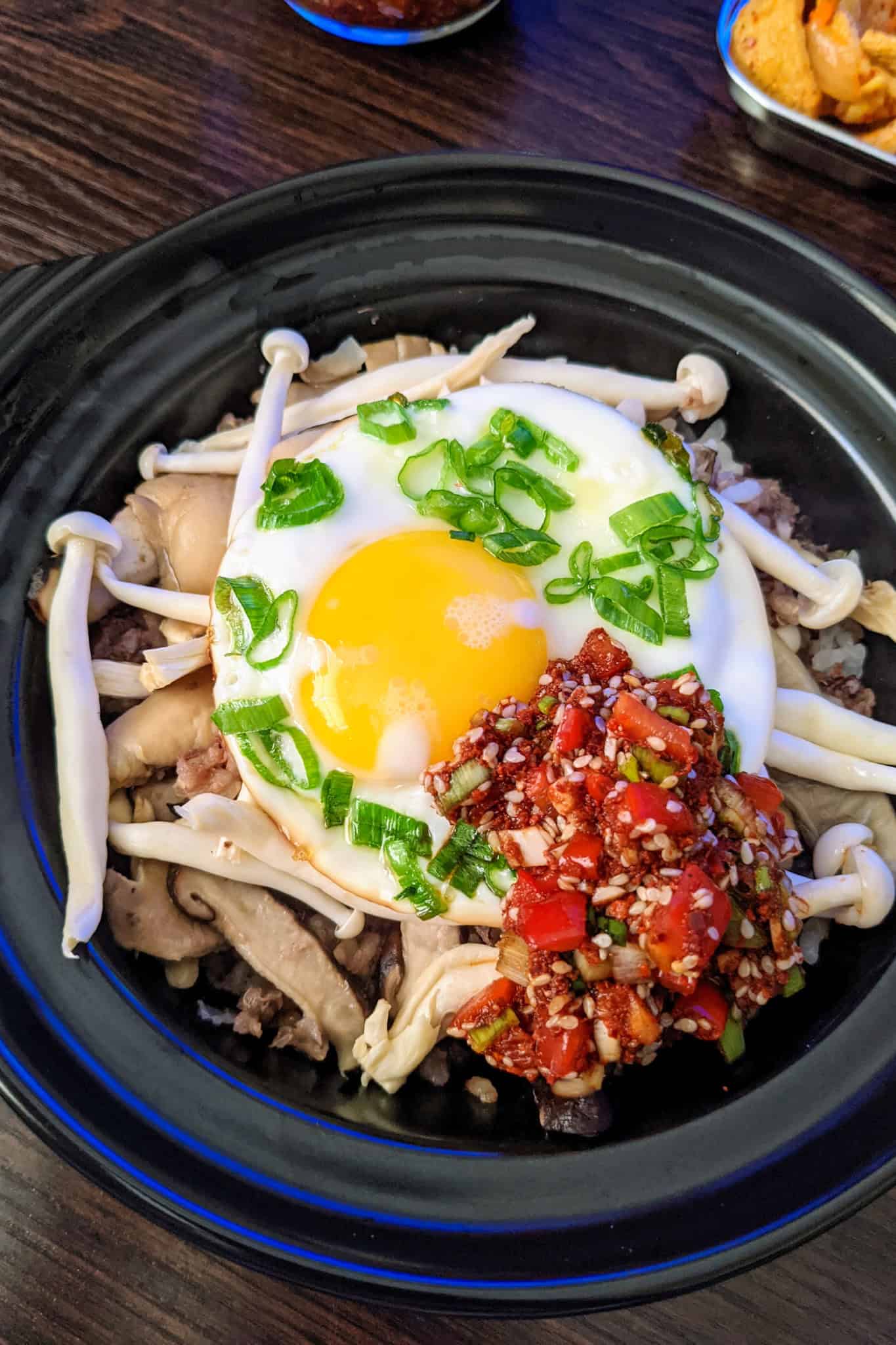 Mushroom and egg Korean Bibimbap bowl with chopped green onions and spicy bibimbap sauce in a stone bowl.