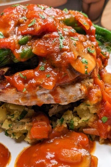 side view of the salmon dish, which is a bed of smashed potatoes topped with a seasoned salmon burger topped with green beans and smothered with a tomato mushroom sauce.
