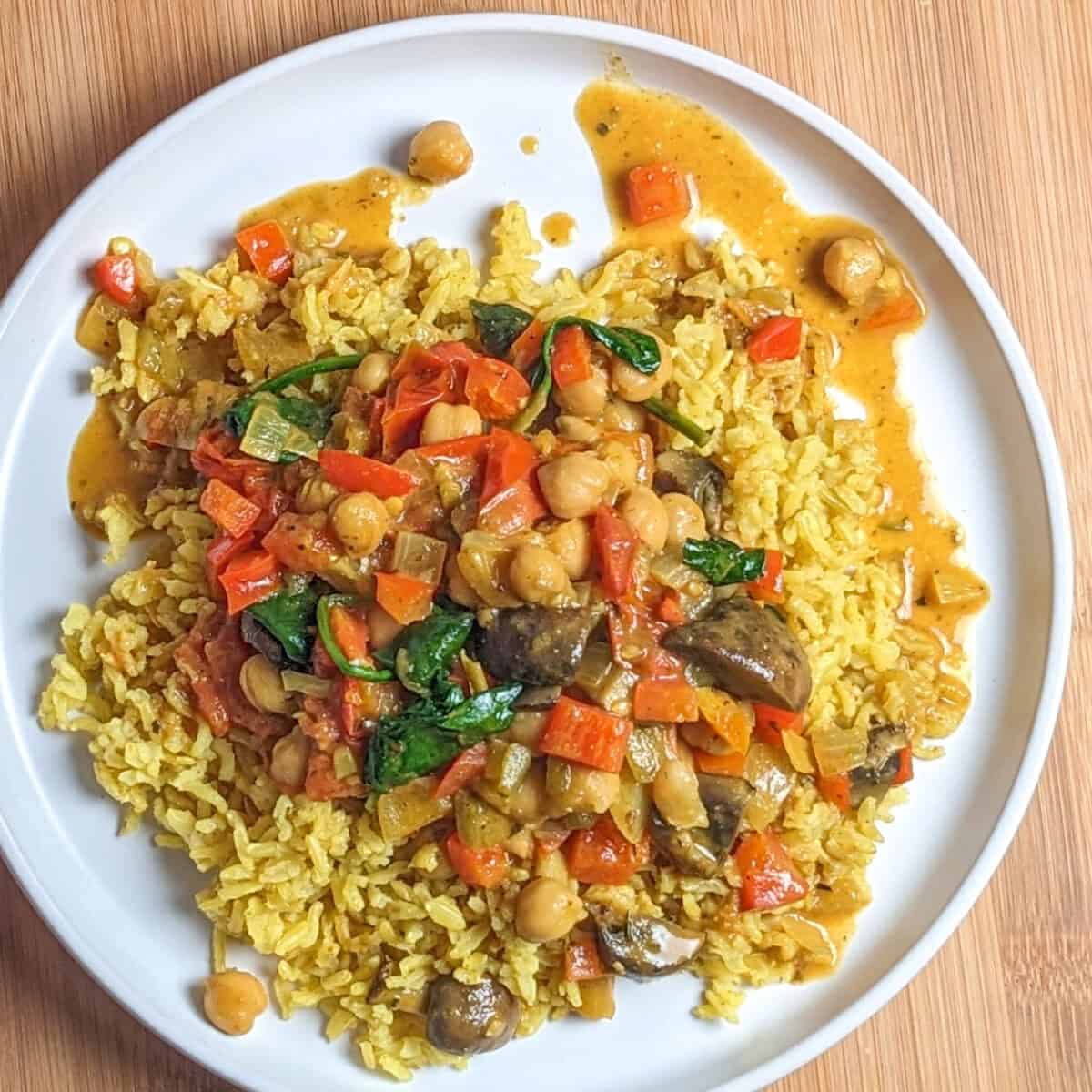 Vibrant chickpeas and vegetables curry over turmeric yellow rice on a white plate.