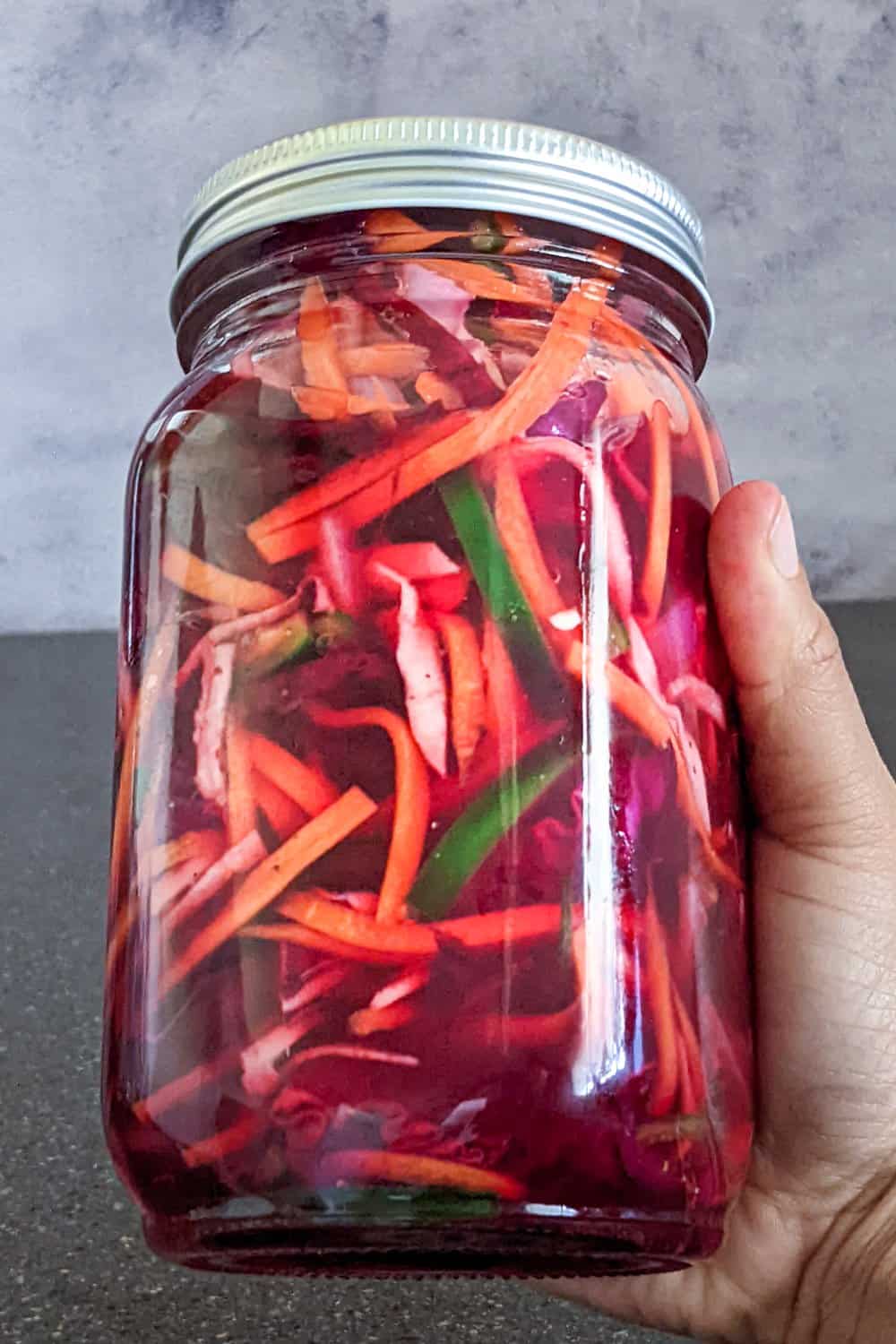 pickled vegetables in red vinegar in a jar being held in one hand