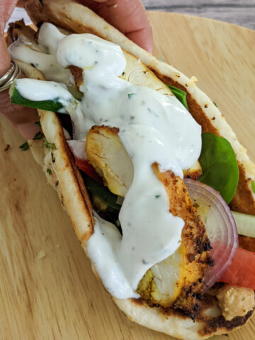 zhug feta hummus chicken wrap on a bamboo plate and folded in hand