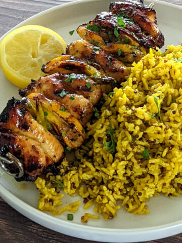 Hot honey lemon chicken skewers with asparagus in between spiced yellow brown rice and half of a lemon