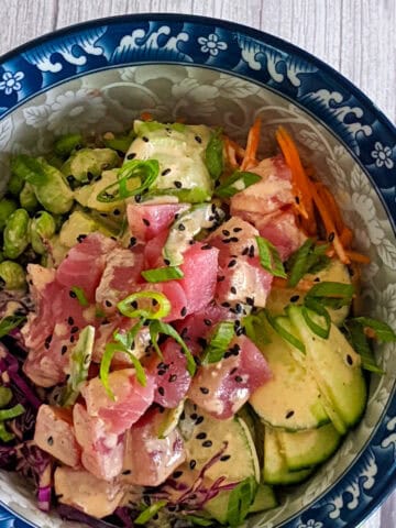 Raw Ahi Tuna surrounded by vegetables with a creamy sauce, decorated with sesame seeds and scallions