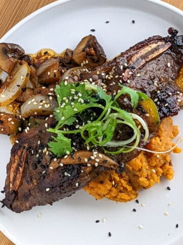 Korean short ribs over mashed sweet potatoes and sautéed vegetables on a white plate