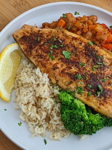 Blackened rainbow trout with spicy chorizo beans, brown rice and garlic broccoli. on a white plate