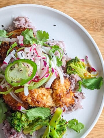 Sweet and spicy sauce coated breaded chicken with multigrain rice, vegetable onion garnish on a white plate.