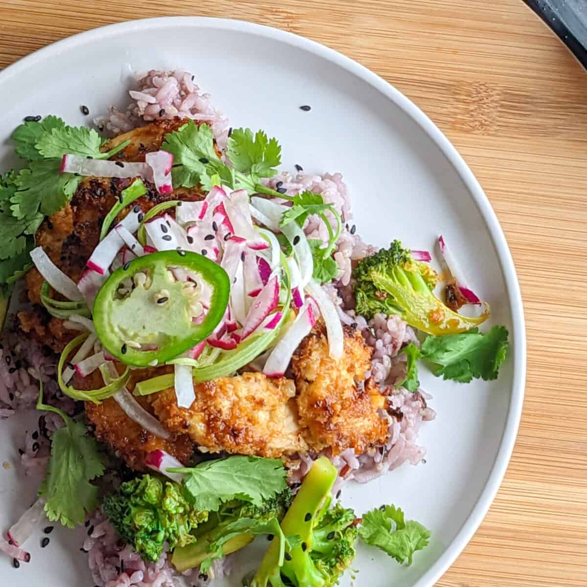 Sweet and spicy sauce coated breaded chicken with multigrain rice, vegetable onion garnish on a white plate.
