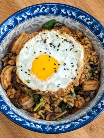 Ramen with seafood and shrimp in a decorative blue bowl with a fried egg with black sesame seeds