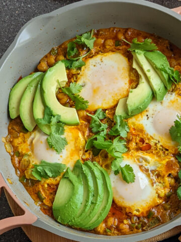 chickepeas in masala curry topped with poached eggs, sliced avocado and cilantro leaves