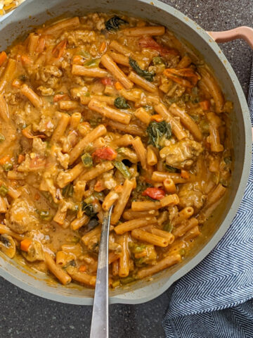 cheesy lentil pasta with ground turkey in a saute pan next a cup of basil