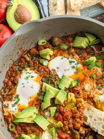 chorizo beans mushroom simmered eggs in a pan topped with avocado and chopped cilantro