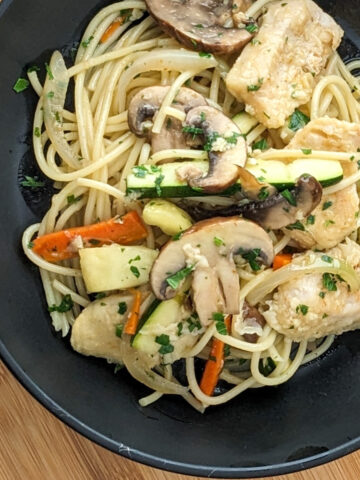 chicken and vegetable spaghetti pasta in black pasta bowl on cutting board