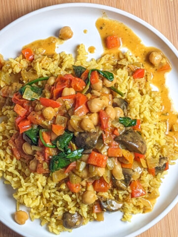 chickpeas and vegetable curry over yellow rice on a white round plate