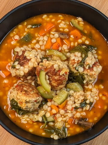Chicken meatball soup with isreali couscous with vegetables in a black bowl