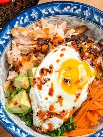 Blue and white bowl with salmon, vegetables, topped with egg and chili sauce