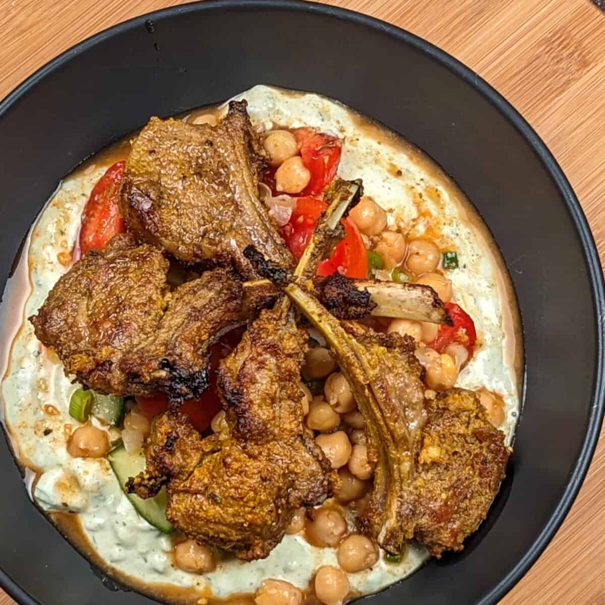 curried lamb jobs on top of chickpea cucumber salad with avocado cream sauce on the bottom
