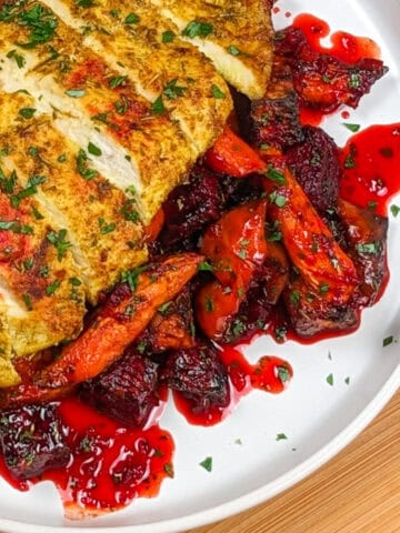 Air fried sliced chicken breast over hot honey glazed root vegetables on a round white plate