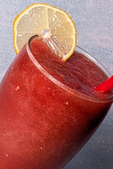 watermelon lemonade in a tall glass with a red straw and fresh sliced lemon wheel on the rim