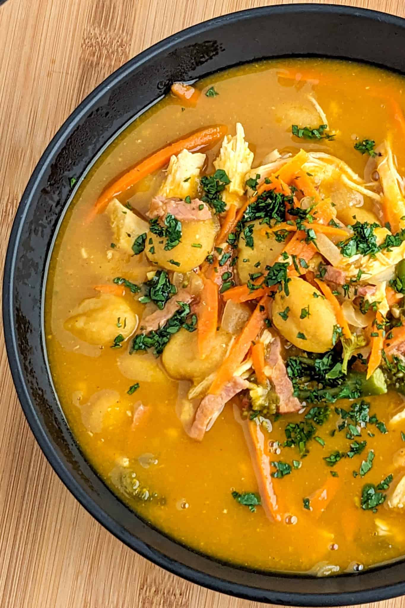 creamy pumpkin broth filled with pumpkin gnocchi, shredded chicken, sliced turkey bacon, vegetables and garnished with fresh herbs in a wide rim soup bowl.