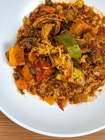 Chicken sweet potato zucchini stew in a tomato base sauce with couscous in a round white pasta bowl on a wooden board