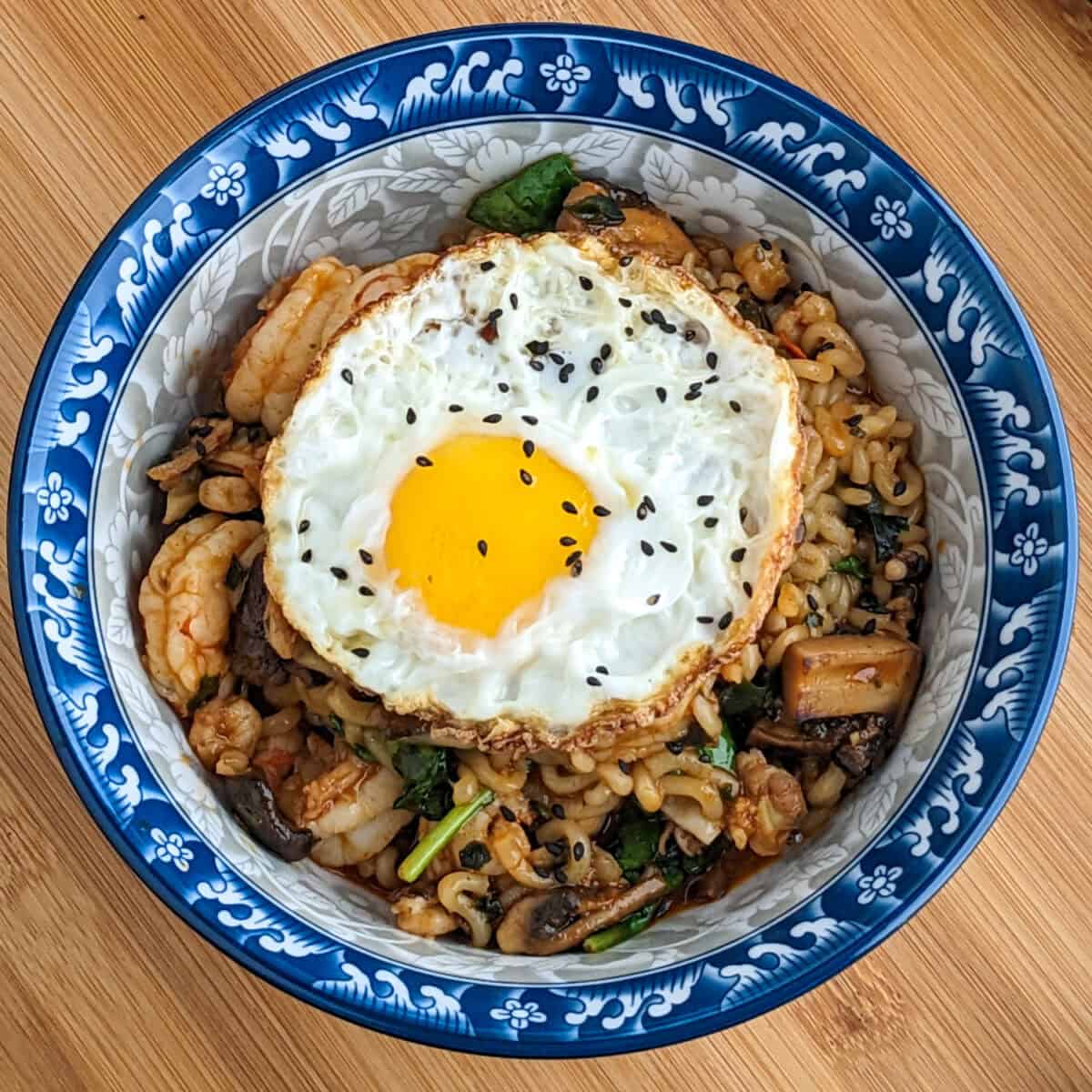 Vibrant seafood noodle bowl topped with a fried egg and black sesame seeds.