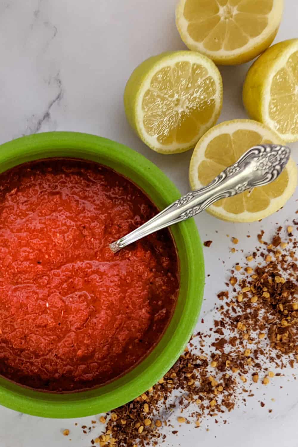 Vibrant harissa sauce with lemon halves and red pepper flakes, perfect for dipping or dressing.