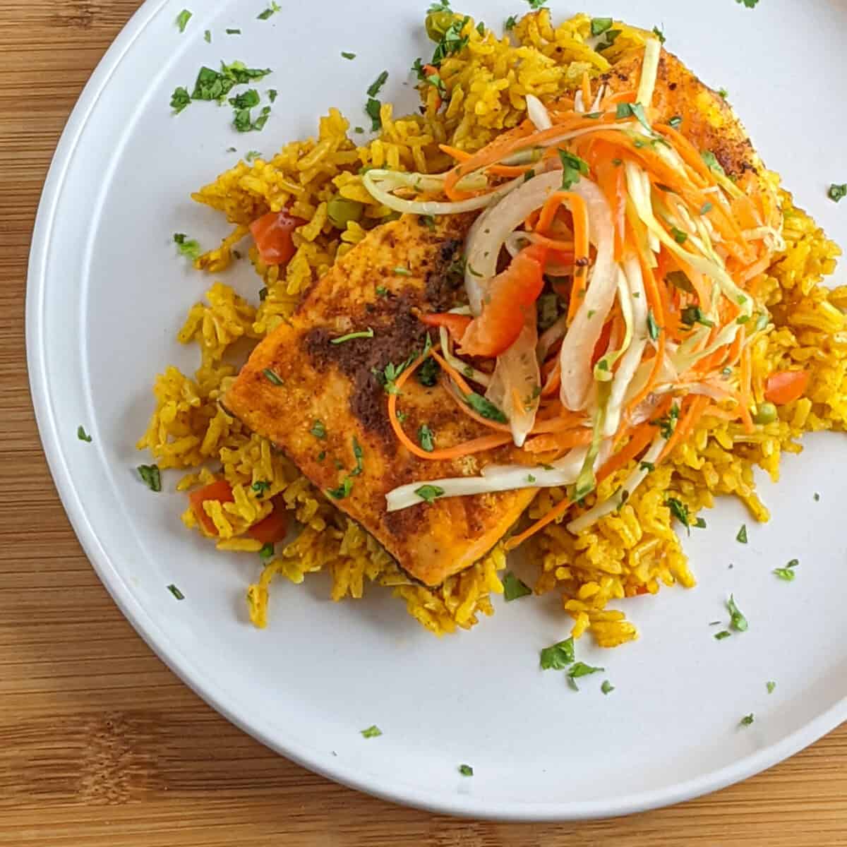 properly cooked golden spiced salmon fillet on fluffy yellow rice with colorful slaw and cilantro garnish.
