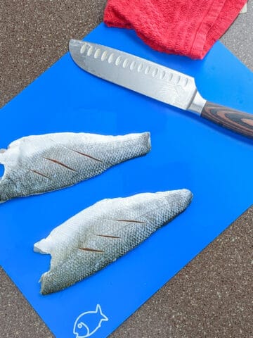 santoku knife on a blue plastic cutting mat marked for fish with two fish filets on it.