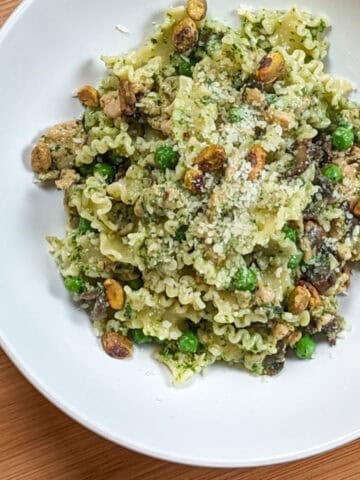 Spicy Pesto Chicken Pasta in a round pasta bowl garnished with grated cheese and pistachios