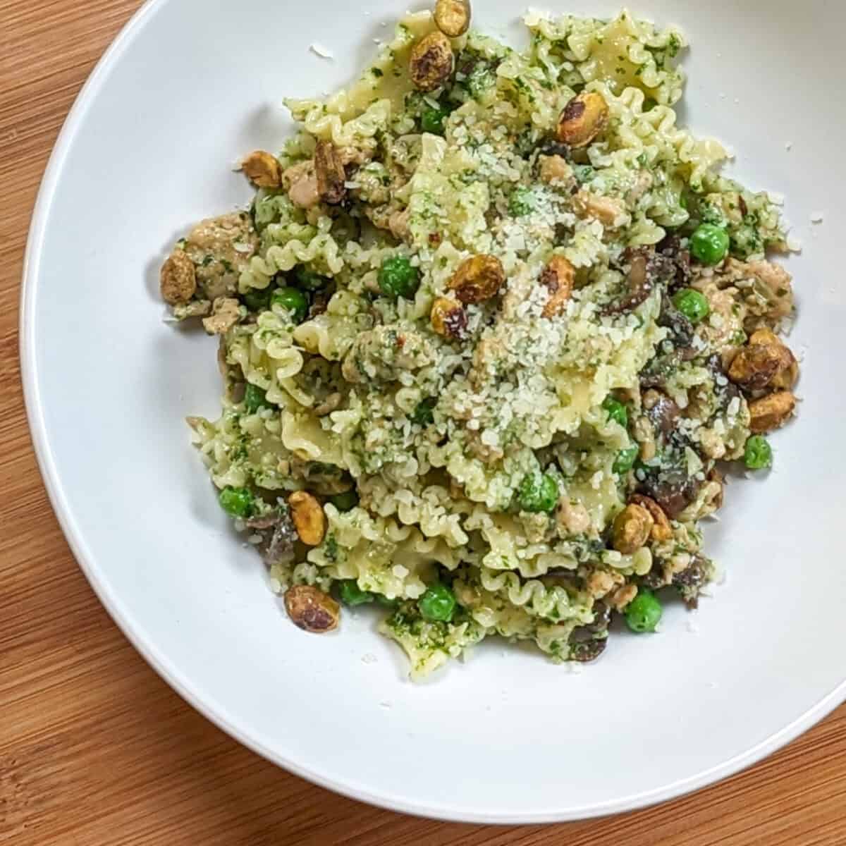 Spicy Pesto Chicken Pasta in a round pasta bowl garnished with grated cheese and pistachios