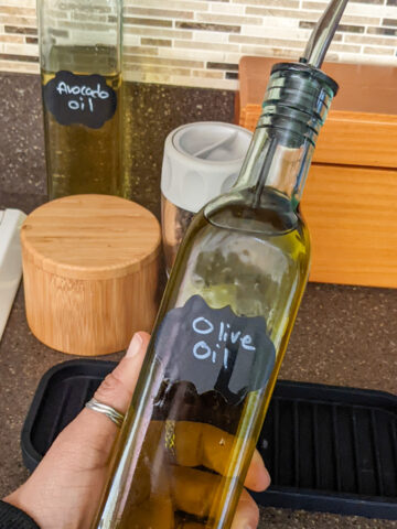 glass bottle with a spout that holds olive oil being held in the hand