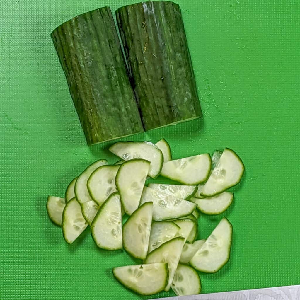 a cucumber halved and thinly sliced on a plastic green cutting board