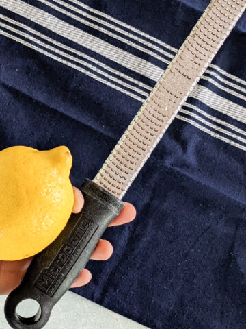 a hand holding a zester and lemon