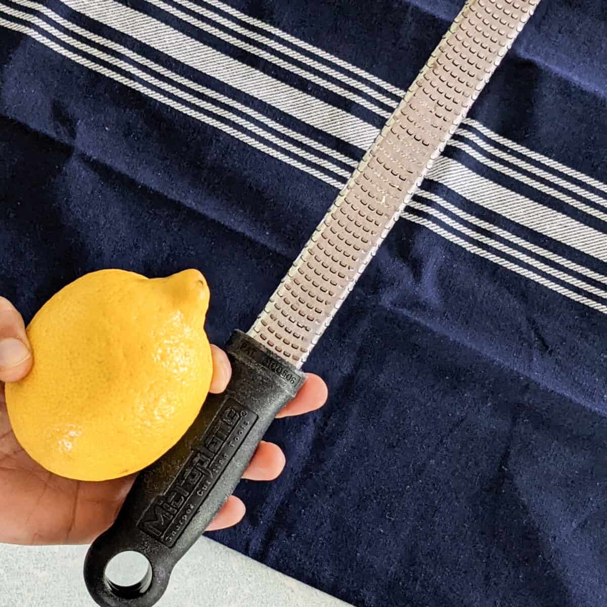 a hand holding a zester and lemon