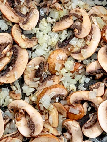sautéed onions and garlic with raw sliced mushrooms in a frying pan for spicy pesto chicken pasta.