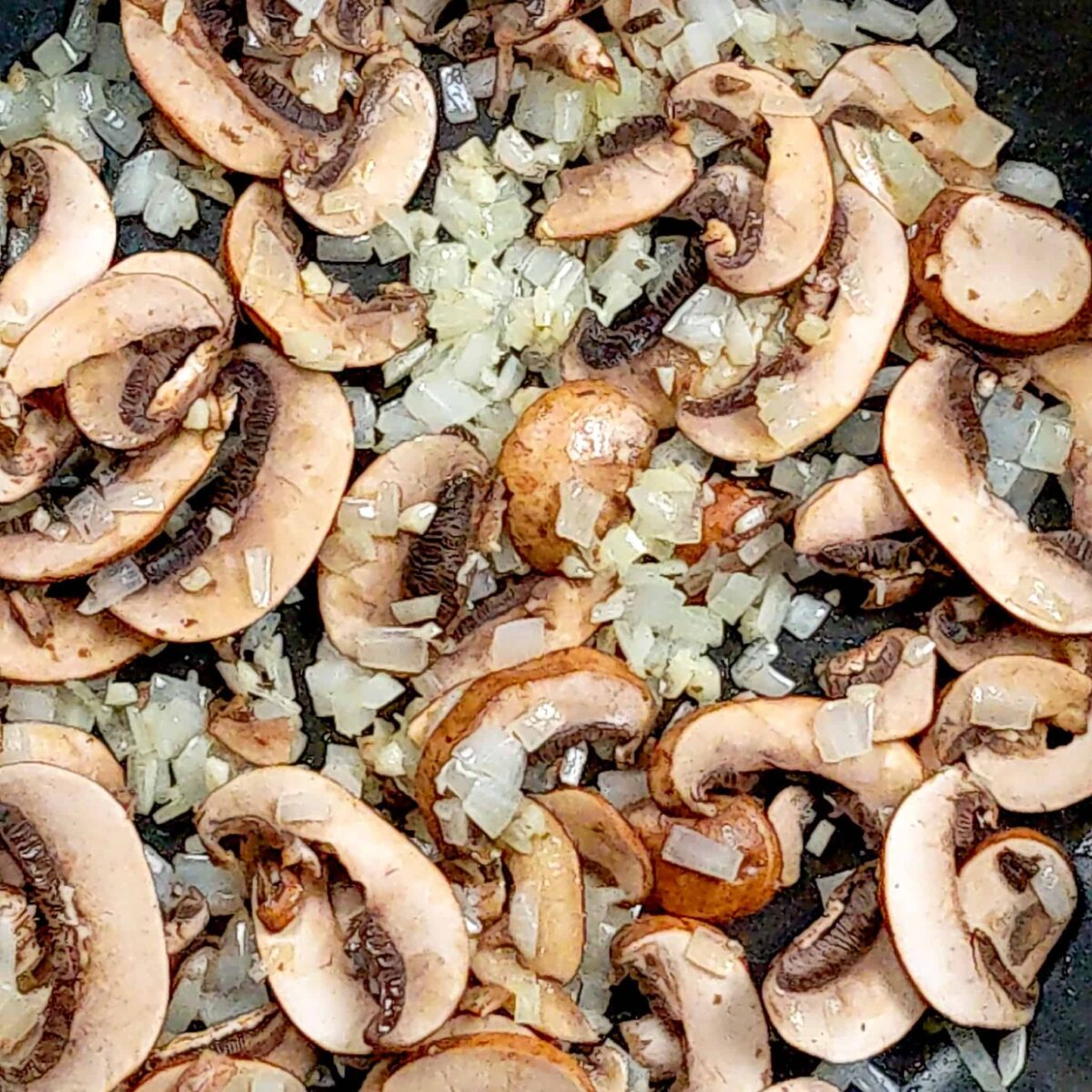 sautéed onions and garlic with raw sliced mushrooms in a frying pan for spicy pesto chicken pasta.