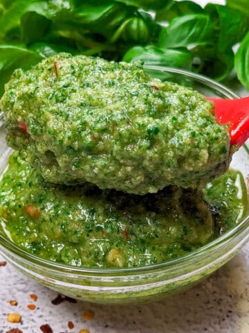 spicy basil pesto in glass bowl with a spoon and fresh basil in the background