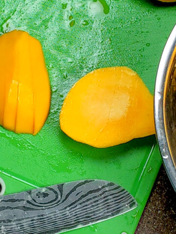 halved mangos on a plastic hard cutting board with a knife