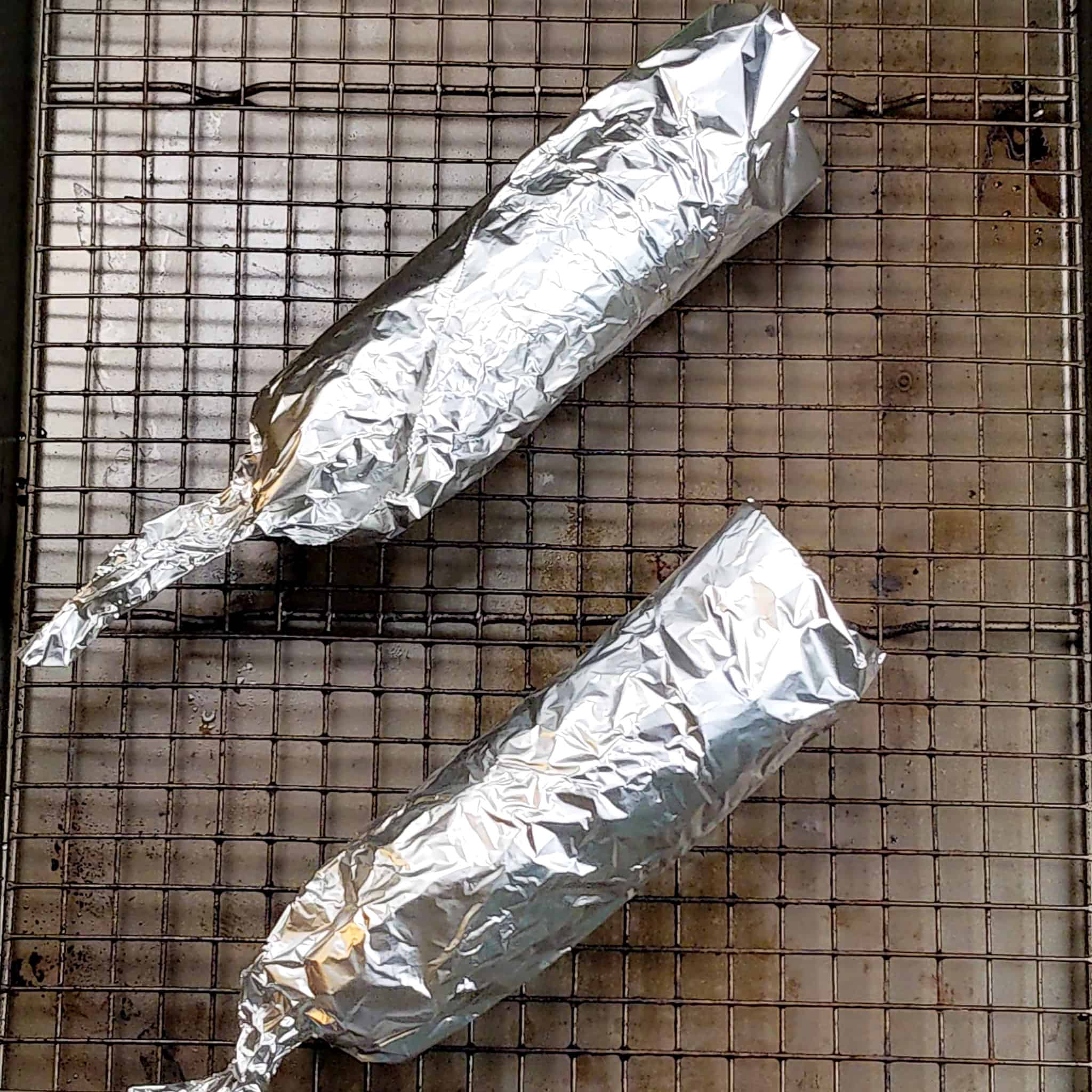 skewered corn on the cob wrapped in aluminum foil on a sheet pan with a rack