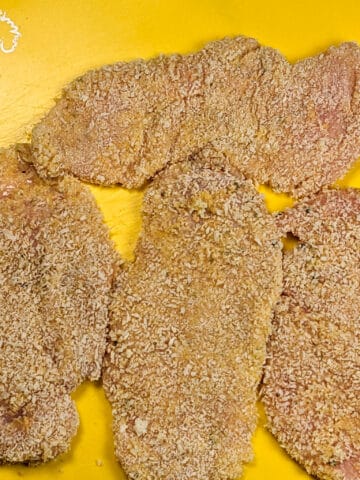 panko breaded chicken cutlets on a yellow cutting board mat.