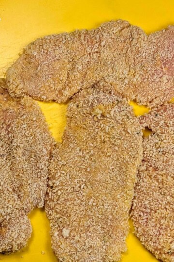 panko breaded chicken cutlets on a yellow cutting board mat.